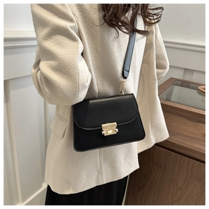 Close-up of black minimalist square bag with gold lock on beige tweed jacket