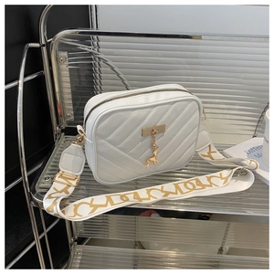 Close-up of white V-quilted camera bag featuring golden deer charm and wide patterned strap