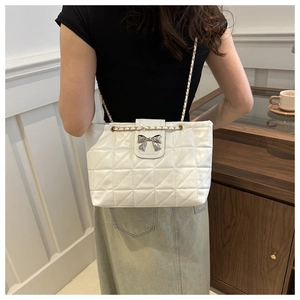 Close-up of white quilted tote bag featuring a silver bow and metal chain strap