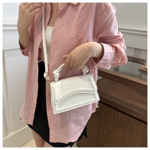 Detail of white square handbag with wavy flap edge and twisted top handle on wood background