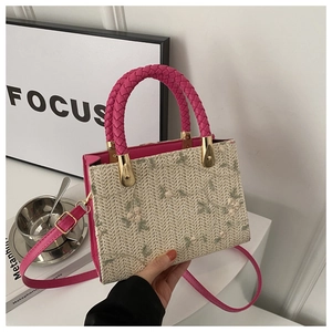 Detailed close-up of straw woven tote with floral embroidery and pink leather strap