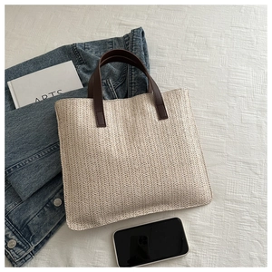 Detail of cream woven tote bag featuring herringbone pattern and brown leather handles