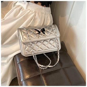 Détail du sac bandoulière argenté matelassé avec fermoir papillon sur fond en cuir