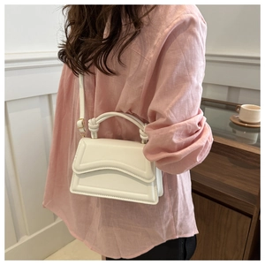 Chic beige handbag with knotted handle and textured flap shown in lifestyle scene