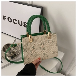 Detail of floral embroidery on a woven straw handbag with a green woven top handle