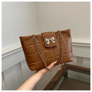 Close-up of brown quilted tote bag featuring silver bow detail and chain strap