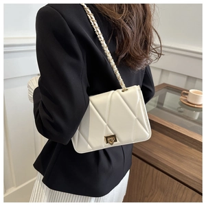 Detail of a creamy white quilted chain bag with elegant gold buckle on model's back