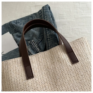 Detailed close-up of herringbone straw weave and brown leather handle with fine stitching