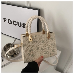 Detail of beige straw handbag featuring exquisite floral embroidery and golden hardware