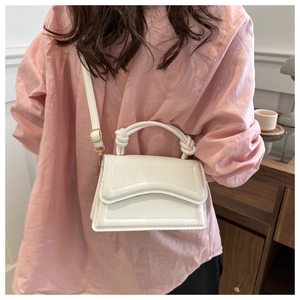 Detail of white minimalist PU leather handbag with woven knot handle and wave pattern