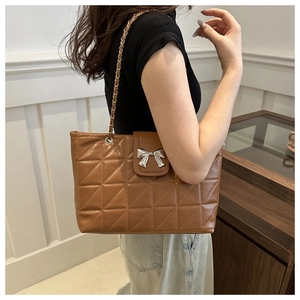 Close-up of brown quilted bag with silver bow buckle worn on a shoulder strap