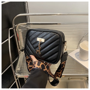 Close-up of black quilted crossbody bag with golden deer charm and wide jacquard strap