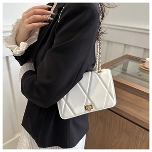 Detail of white quilted chain bag featuring a gold square twist lock and leather-woven strap