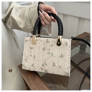 Detail of beige straw handbag with floral embroidery and black woven handle in hand