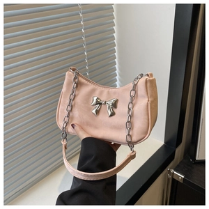 Detail of pink faux suede shoulder bag featuring a silver metal bow and chunky chain