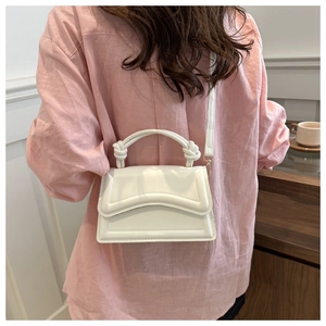 Detail of white PU leather crossbody bag featuring twist knot handle and geometric stitching