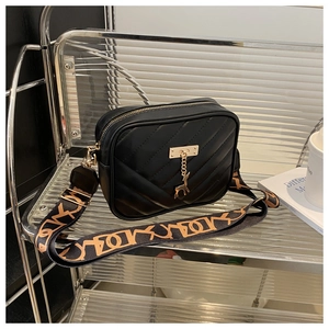 Detail of black quilted crossbody bag with metal deer charm and wide letter strap