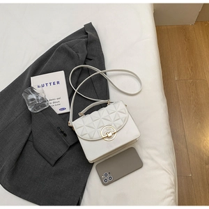 Detail of white quilted crossbody bag featuring a golden round lock on elegant bedding