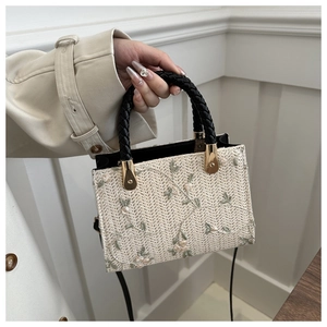 Detail of floral embroidery on a woven handbag with straw texture and green vines
