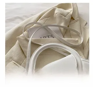 Dettaglio della borsa bianca con manico circolare in metallo su sfondo blazer beige