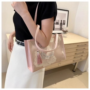 Detail of pink embroidered tote bag with floral patterns and a silk tassel charm
