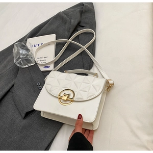 Detail of white quilted crossbody bag with golden clasp on a gray blazer backdrop