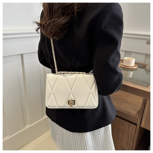 Detail view of a white quilted crossbody bag with gold chain strap and metal lock