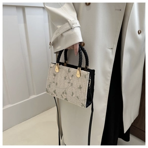 Detail of floral embroidery on a beige woven straw handbag with black leather side panels