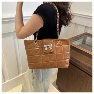 Macro detail of brown quilted tote bag featuring silver bow accent and chain strap