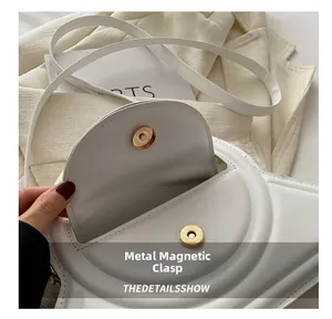 Dettaglio della fibbia magnetica dorata su una borsa a tracolla bianca minimalista