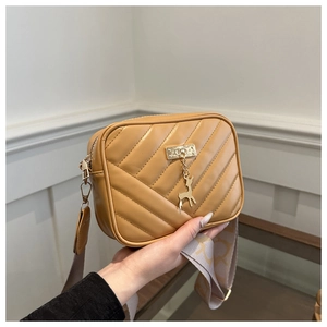 Close-up of bright yellow quilted crossbody bag featuring a golden deer charm and wide strap