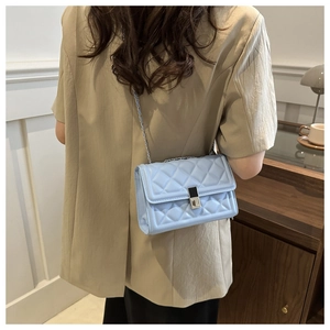 Detail view of light blue quilted chain bag with silver lock on a model's shoulder