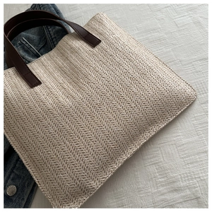 Detail of cream woven tote bag with brown leather handles and herringbone pattern