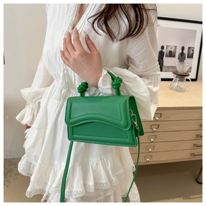 Detail view of bright green handbag with knot handle and curved textured stitching