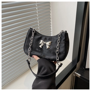 Close-up of black nylon shoulder bag with a large silver metal bow and chain strap detail