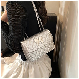 Détail d'un sac bandoulière argenté matelassé avec boucle papillon et bandoulière chaîne