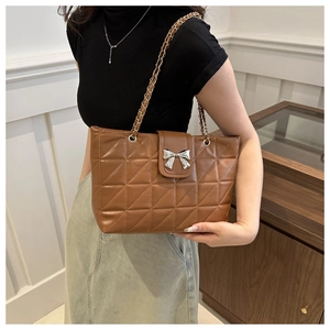 Close-up of brown quilted bag with silver bow buckle and chain strap on shoulder