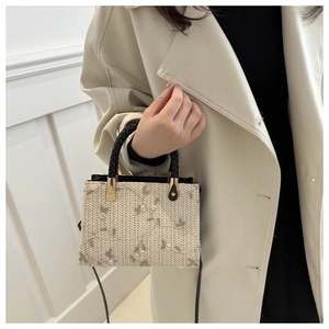 Detail of cream straw bag featuring floral embroidery and round black top handle