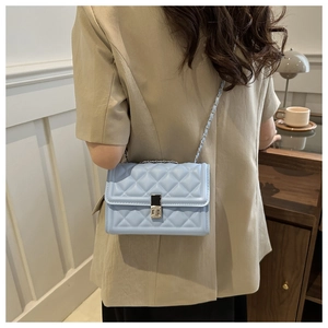Detail view of a light blue quilted crossbody bag with a metal chain strap and lock