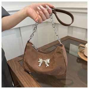 Detailed view of brown baguette bag featuring a silver metal bow and chain handle