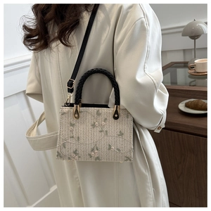 Detail of hand-woven straw tote bag with delicate floral embroidery and black handles