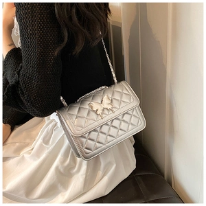 Détail de la texture matelassée argentée et du fermoir papillon 3D sur le sac à chaîne