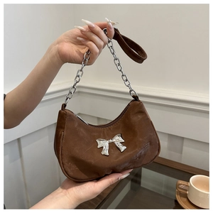 Detail of a brown canvas crescent bag with silver bow buckle and chunky metal chain