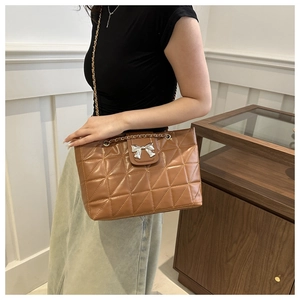 Detail of a brown quilted tote bag with a silver bow clasp and chain shoulder strap