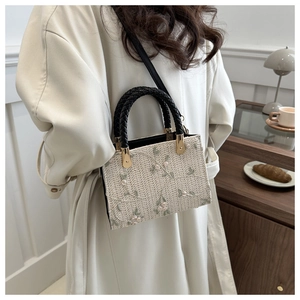 Detail of floral embroidery on a woven straw handbag with adjustable black strap