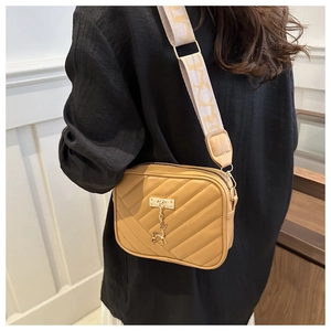 Detail of yellow quilted crossbody bag featuring a golden deer charm and wide jacquard strap