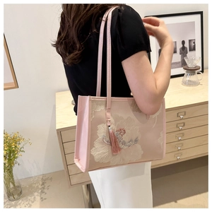 Détail du sac cabas rose avec broderie florale et pompon en soie suspendu sur le côté