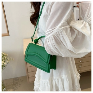 Close-up of bright green handbag featuring a wavy flap and knotted top handle design