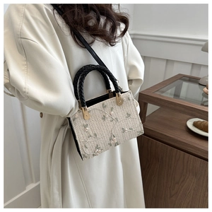 Detail of beige straw handbag featuring pastel floral embroidery and woven handles