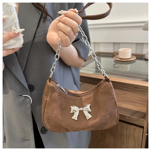 Detail of brown hobo bag featuring large silver metal bow and chunky chain strap